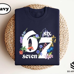 A navy blue t-shirt with a floral design and the number "67" printed on it, placed on a woven basket.