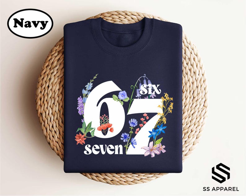 A navy blue t-shirt with a floral design and the number "67" printed on it, placed on a woven basket.