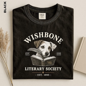 A black t-shirt with a graphic design featuring a dog holding a book, along with text that reads "Wishbone Literary Society" and "EST. 1995".