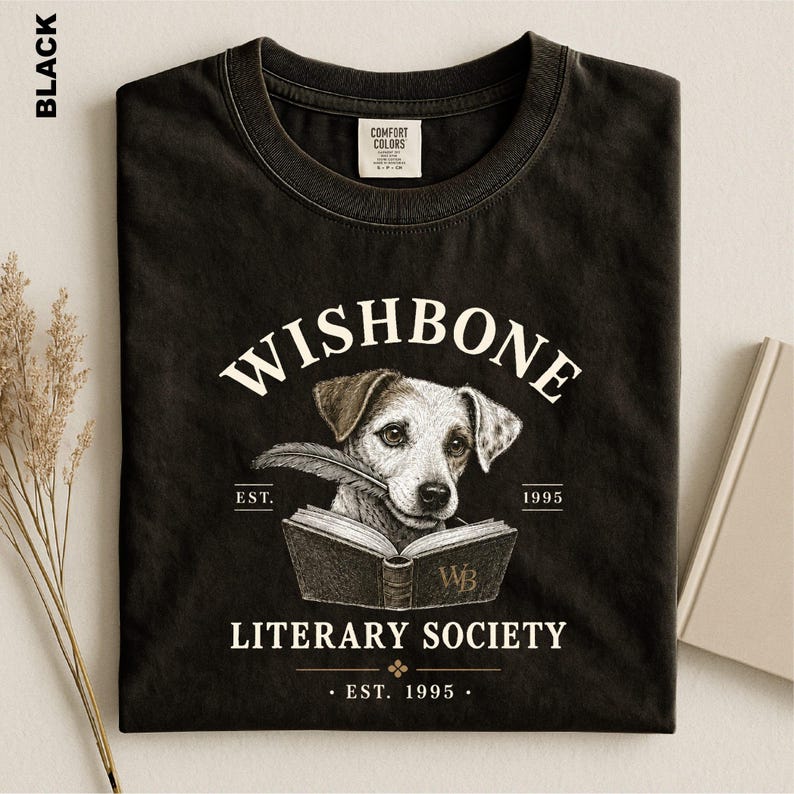A black t-shirt with a graphic design featuring a dog holding a book, along with text that reads "Wishbone Literary Society" and "EST. 1995".
