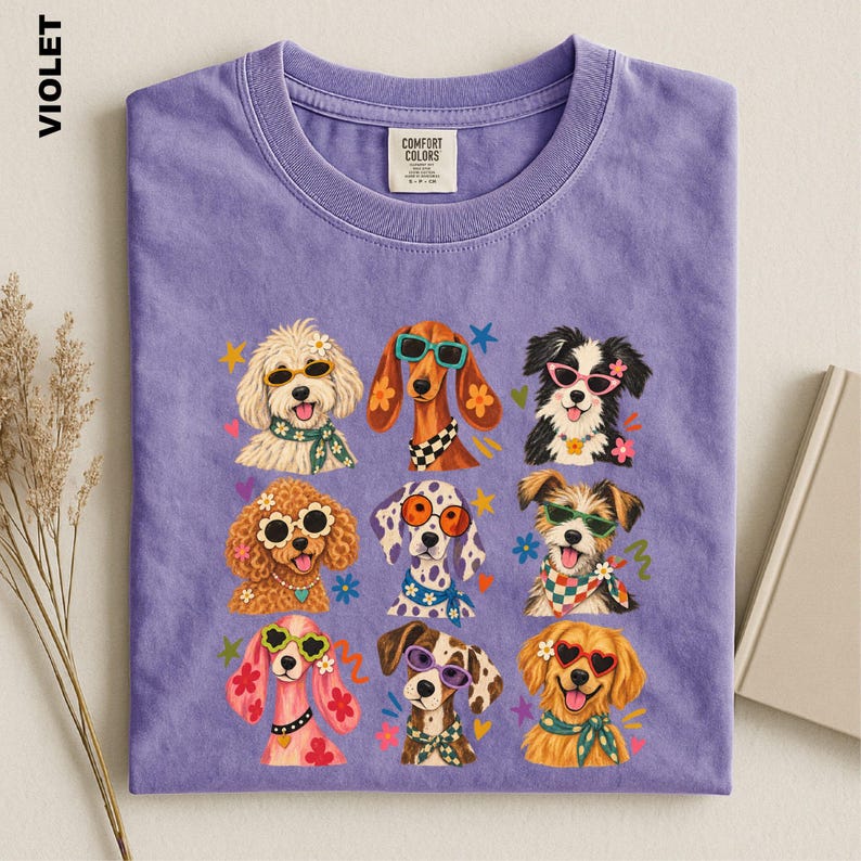 Puede incluir: Una camiseta violeta con un estampado gr&aacute;fico de nueve razas de perros diferentes, cada una con gafas de sol coloridas y pa&ntilde;uelos estampados. La camiseta tiene cuello redondo y una etiqueta de la marca Comfort Colors en el interior.