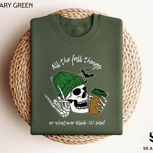 May include: A green t-shirt with a skeleton wearing a green beanie and holding a cup of coffee. The text on the shirt reads "All the fall things or whatever blink-182 said!"