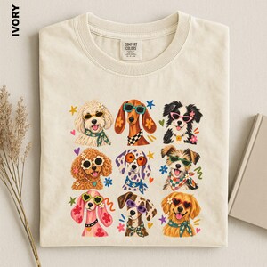 Puede incluir: Una camiseta de cuello redondo color marfil con un estampado gr&aacute;fico de nueve perros que llevan gafas de sol coloridas y pa&ntilde;uelos estampados. Los perros est&aacute;n dispuestos en una cuadr&iacute;cula, cada uno con colores de pelaje y estilos distintos.