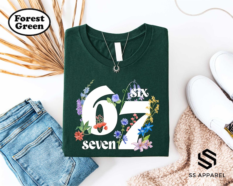 a green t-shirt with the number "67" printed on it, surrounded by various clothing items and accessories, including jeans, a pair of sneakers, and a sweater.