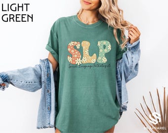 May include: A light green t-shirt with a floral design spelling out "SLP" and the text "Speech Language Pathologist".