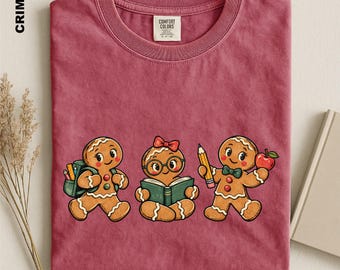 Op de afbeelding: Een karmozijnrood T-shirt met ronde hals en een afbeelding van drie peperkoekfiguurtjes. Eén draagt een rugzak, één leest een boek met een bril en strik, en één houdt een potlood en een appel vast. Het label aan de binnenkant toont Comfort Colors.