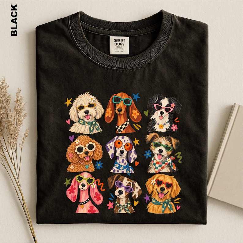Puede incluir: Una camiseta negra con un estampado gr&aacute;fico de nueve razas de perros diferentes, cada una con gafas de sol coloridas y pa&ntilde;uelos o collares estampados. El dise&ntilde;o incluye peque&ntilde;os detalles de estrellas y flores. La camiseta tiene una etiqueta Comfort Colors.