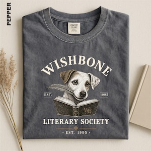 A gray t-shirt with a graphic design featuring a dog holding a book, along with text that reads "Wishbone Literary Society" and "EST. 1995".
