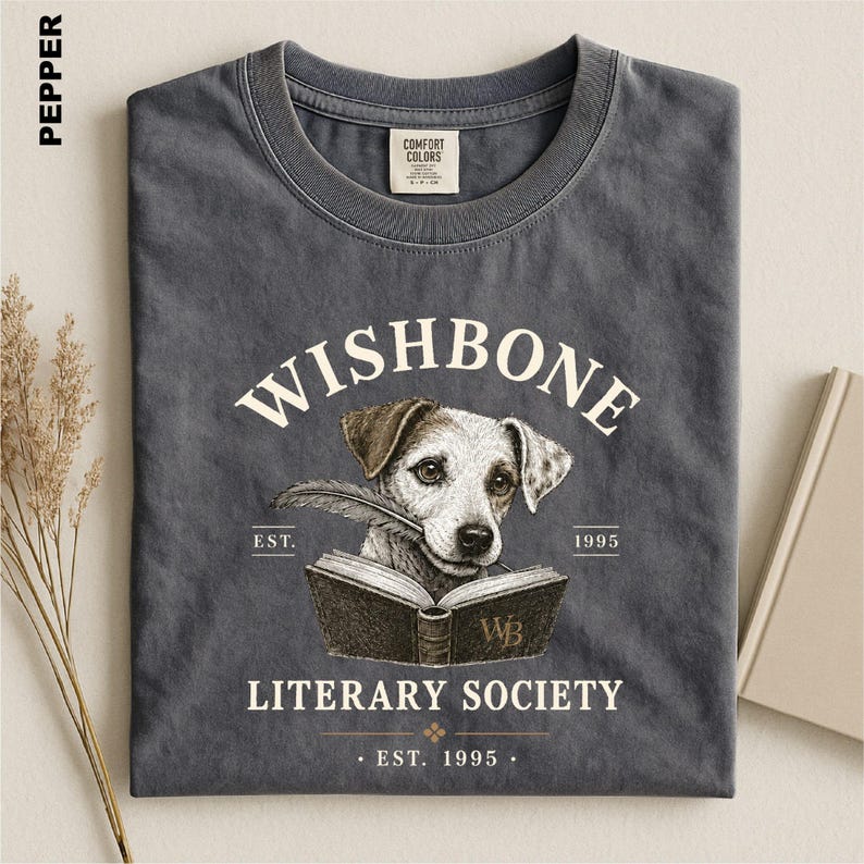 A gray t-shirt with a graphic design featuring a dog holding a book, along with text that reads "Wishbone Literary Society" and "EST. 1995".