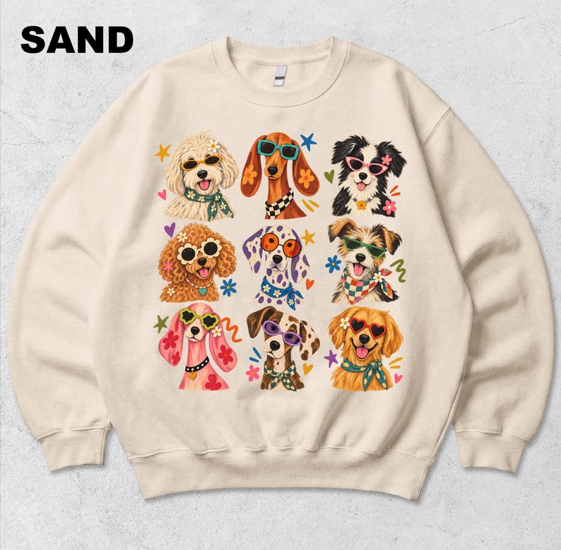 Puede incluir: Una sudadera de cuello redondo color arena con un estampado gr&aacute;fico de nueve razas de perros diferentes. Cada perro lleva gafas de sol coloridas y un pa&ntilde;uelo o collar estampado. La palabra SAND est&aacute; impresa en negro en la esquina superior.