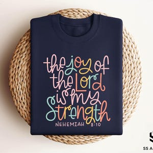 May include: Navy blue t-shirt with the text "the joy of the Lord is my strength" in colorful lettering. The text "Nehemiah 8:10" is printed below the main text.