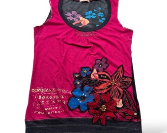 May include: A sleeveless magenta top with a dark gray neckline and hem. The top features floral appliqués in red, blue, and black, with gold text on the lower left. The neckline has a floral design.