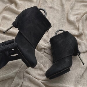 May include: A pair of black ankle boots featuring a front zipper closure, a rounded toe, and a slim metallic stiletto heel. Each boot includes a flexible metal spring shoe tree insert at the top opening to maintain the shape of the footwear.