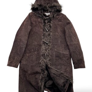 May include: A brown suede coat with a hood and faux fur trim. The long coat features a toggle closure and two front pockets. The hood and front trim are lined with faux fur. The coat is a dark brown color.