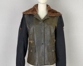 May include: A jacket featuring a distressed olive green body with black sleeves and a brown faux fur collar. The front includes a button-down closure, two flap pockets at the waist, and a small embroidered emblem on the right chest area.