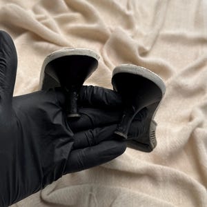May include: A pair of shoes featuring black kitten heels and white soles. The heels are narrow and tapered, showing signs of wear on the base. The white soles are rounded at the heel area, providing a contrast to the black heel structure.