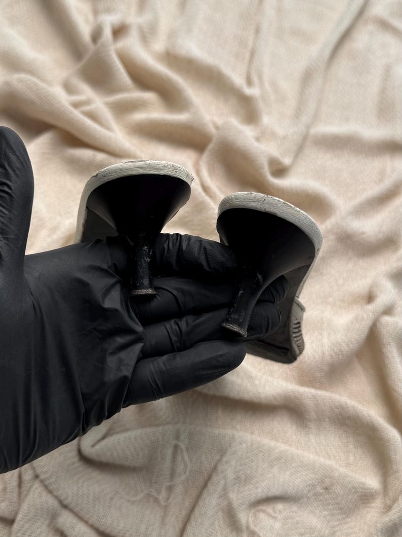 May include: A pair of shoes featuring black kitten heels and white soles. The heels are narrow and tapered, showing signs of wear on the base. The white soles are rounded at the heel area, providing a contrast to the black heel structure.