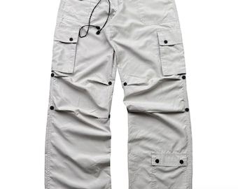 Könnte beinhalten: Hellgraue Cargohose mit mehreren Taschen und schwarzen Knöpfen. Die Hose hat einen Kordelzug in der Taille und eine lockere Passform. Der Stoff scheint leicht und für Freizeitkleidung geeignet zu sein.