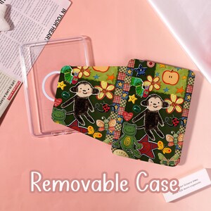 Puede incluir: Una funda de teléfono extraíble transparente con un inserto estampado. El inserto presenta un mono de dibujos animados, flores, estrellas y otros elementos lúdicos. El texto "Removable Case" es visible.