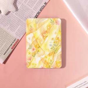 May include: A rectangular tablet case featuring a soft yellow and white watercolor wash background with scattered small heart shapes and delicate botanical illustrations of pink, yellow, white, and blue flowers with green leaves and stems.