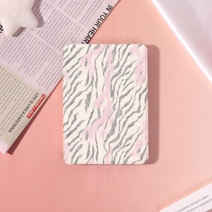 Op de afbeelding: Een rechthoekig elektronisch leesapparaat met een beschermhoes met een witte achtergrond, een grijs zebrapatroon en zachte roze aquarelachtige accenten die verticaal over het oppervlak zijn verdeeld.