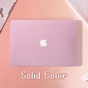 May include: A light pink laptop with the Apple logo centered on the lid. The words "Solid Color" are displayed in white script at the bottom of the image. The laptop is on a gradient background of pink and peach.