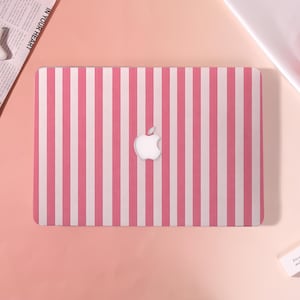 May include: A pink and white striped laptop cover with the Apple logo in the center. The cover has a vertical stripe pattern. The background is a gradient of pink.
