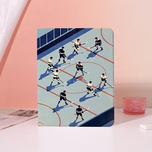 May include: A rectangular tablet case featuring an illustration of a hockey game in progress on a light blue rink surface. Nine hockey players in dark and light uniforms are positioned across the ice, each holding a stick with shadows cast below.