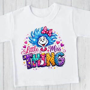 May include: White t-shirt with a colourful graphic of a character with blue hair, a pink bow, and the words "Little Miss Thing." The design includes hearts, stars, and a crown, creating a playful and vibrant look.