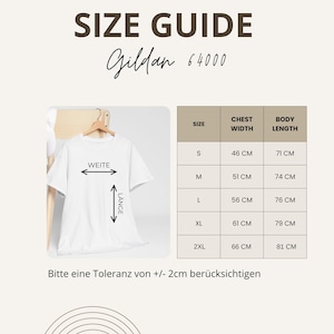 May include: A white t-shirt hanging on a wooden hanger, with a size guide chart. The chart lists sizes S to 2XL, chest width in centimeters, and body length in centimeters. The text "SIZE GUIDE" and "Gildan 64000" are at the top.