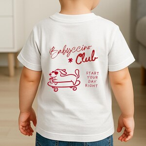 Peut inclure: T-shirt blanc avec un motif rouge au dos. Le motif comprend les mots "Babyccino Club" et un chien de dessin anim&eacute; sur un skateboard tenant une tasse. L'expression "Start Your Day Right" est &eacute;galement imprim&eacute;e sur le t-shirt.