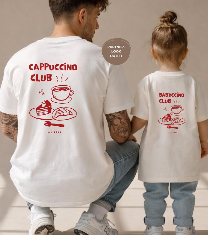 May include: White t-shirts with red graphics. One shirt reads "Cappuccino Club" with coffee cup, cake, and croissant illustrations. The other shirt says "Babyccino Club" with similar graphics. Both shirts have "since 2023" text.