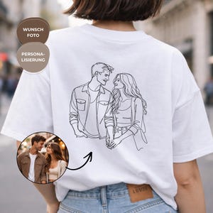 Op de afbeelding: Wit T-shirt met een lijntekening van een stel, en een kleine cirkelvormige foto van het stel. Het shirt heeft ook de woorden "Wunsch Foto" en "Personalisierung" in een bruine cirkel.