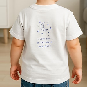 May include: White t-shirt with a blue crescent moon and star design. The text "I LOVE YOU TO THE MOON AND BACK" is printed below the graphic. The shirt is worn by a child.