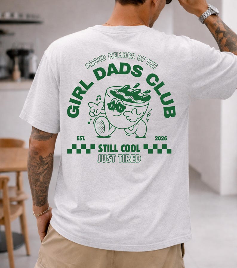 May include: Light gray t-shirt with a green graphic on the back. The graphic reads "GIRL DADS CLUB" with a cartoon character and the text "EST. 2026 STILL COOL JUST TIRED".