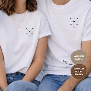May include: White t-shirts featuring a black arrow and heart design, with the date "29 01 2021" and initials. The shirts are worn by two people, with the design on the chest.