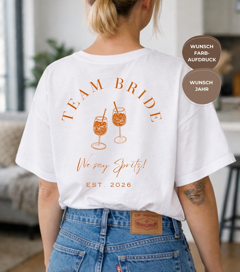 May include: White t-shirt with the words "TEAM BRIDE" in a burnt orange color, along with two spritz drink illustrations. The text "We say Spritz!" and "EST. 2026" are also printed on the shirt.