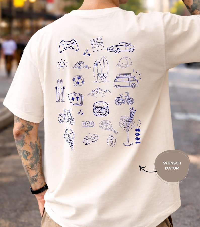 May include: An off-white t-shirt featuring a back print of various blue line-art icons including a game controller, car, surfboard, van, bicycle, burger, ice cream, and the word DAD. The number 1998 is printed vertically near the bottom right.