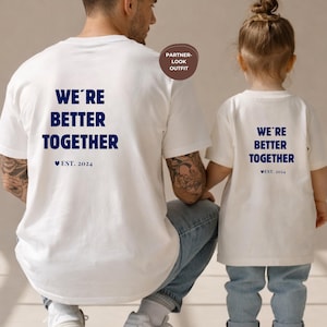 以下が含まれることがあります： ネイビーブルーの「WE'RE BETTER TOGETHER」と「EST. 2024」の文字が入った白いTシャツ2枚。大人と子供が着ており、お揃いの服を示唆しています。画像には「PARTNER-LOOK OUTFIT」のラベルも含まれています。