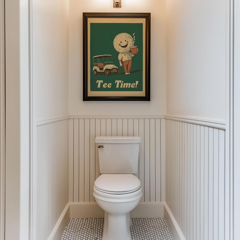 May include: A white toilet with a white and black tiled floor in a bathroom with white wainscoting. A framed poster with a green background and a cartoon golf ball character holding a cup of coffee and riding in a golf cart. The poster says "Tee Time!"
