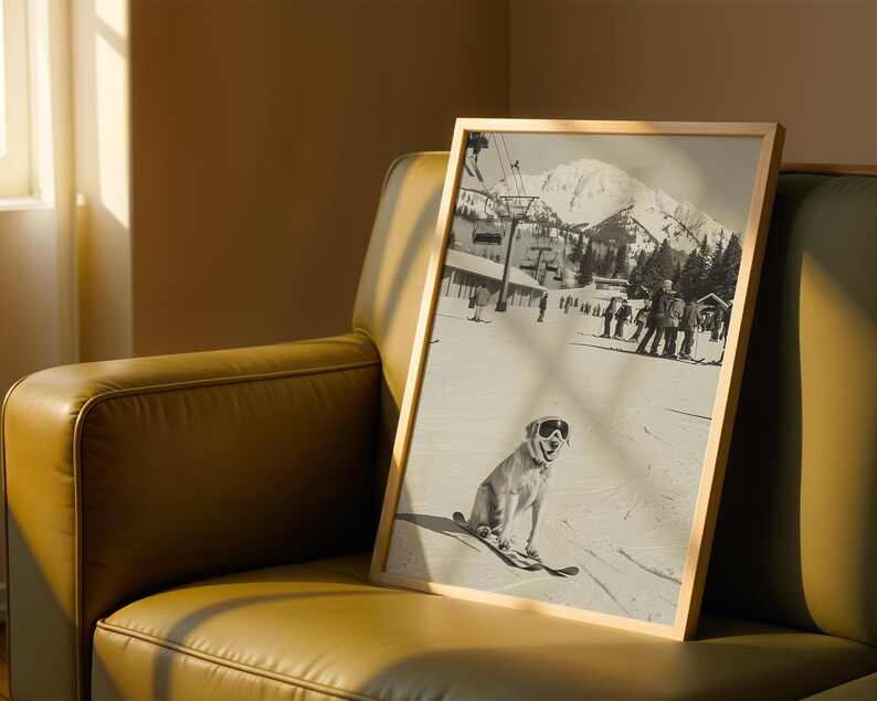 May include: A framed black and white photograph of a dog wearing ski goggles and skis, sitting on a snowy slope. The background shows a ski resort with skiers, a ski lift, and a mountain range. The frame is a light wood color.