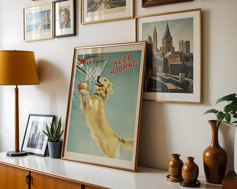 May include: A framed print featuring a golden retriever playing basketball, with the text "KEEP HOOPING" in red. The dog is jumping to dunk the ball. The print is in a gold frame and is displayed with other framed art.