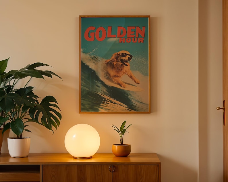 May include: A framed poster with the words "GOLDEN HOUR" in red letters, featuring a dog wearing sunglasses surfing a wave. The poster is displayed above a wooden cabinet with a round, glowing lamp and a potted plant.