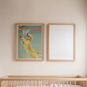 May include: Two framed prints hang above a wooden crib. One print features a golden retriever playing basketball with the text "KEEP HOOPING". The second frame is empty. The room has a neutral color palette.