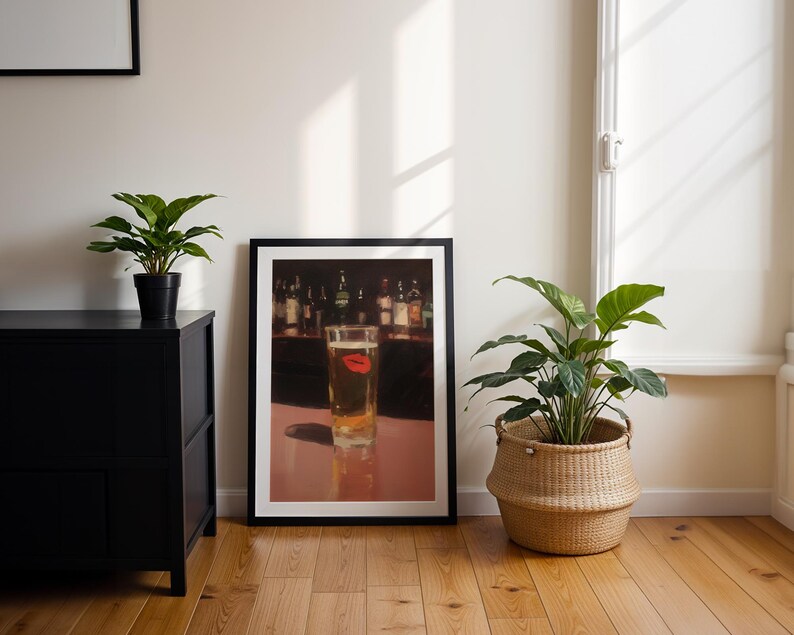 Puede incluir: Una impresi&oacute;n enmarcada que muestra un vaso de cerveza con una marca de l&aacute;piz labial rojo. La impresi&oacute;n est&aacute; en un marco negro, sobre un suelo de madera. Un armario negro y plantas en macetas tambi&eacute;n est&aacute;n en la habitaci&oacute;n.