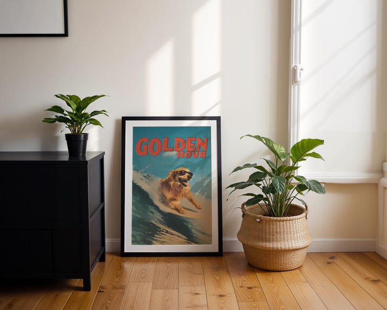 May include: A framed poster with the words "GOLDEN HOUR" in red text. The poster features a golden retriever dog wearing sunglasses surfing a wave. The poster is in a black frame and is leaning against a white wall.