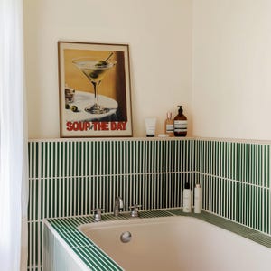 Peut inclure: Une baignoire blanche avec un carrelage vert et blanc. Au-dessus de la baignoire, il y a un imprim&eacute; encadr&eacute; d'un verre &agrave; martini avec des olives. L'impression dit "Soup of the Day". Il y a trois bouteilles de produits de toilette sur l'&eacute;tag&egrave;re au-dessus de la baignoire.