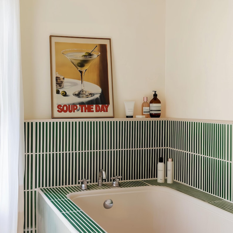 Peut inclure: Une baignoire blanche avec un carrelage vert et blanc. Au-dessus de la baignoire, il y a un imprim&eacute; encadr&eacute; d'un verre &agrave; martini avec des olives. L'impression dit "Soup of the Day". Il y a trois bouteilles de produits de toilette sur l'&eacute;tag&egrave;re au-dessus de la baignoire.