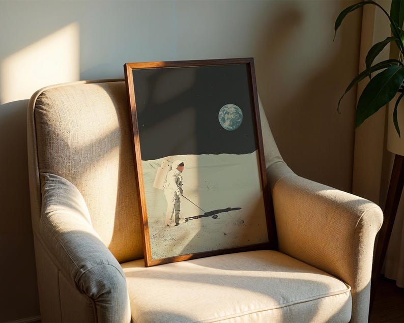 May include: A framed print of an astronaut in a spacesuit walking on the moon, with a small planet in the background. The print is in a brown wooden frame and is hanging on a beige wall.