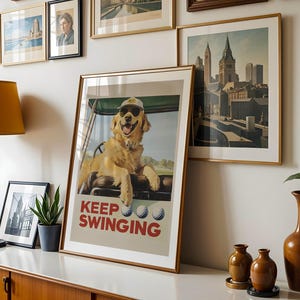 May include: A poster with a golden retriever dog wearing a golf hat and sitting in a golf cart. The poster has the text "Keep Swinging" and three golf balls.